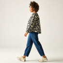 Side view of model walking in the cream and black floral quilted jacket with blue jeans and cream trainers.