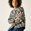 Seated close-up of the cream quilted jacket with black floral pattern, showing the quilted texture and sleeve detail.