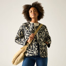 Model wearing a cream quilted jacket with a black floral pattern and contrast piping, carrying a beige crossbody bag over jeans.