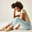Model seated wearing light blue chambray trousers with a beige T-shirt and beige clogs, showing the tapered leg and cuffed hem.