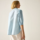 Back view of the model wearing the light blue pinstripe blouse, showing the longer back hem and three-quarter sleeves.