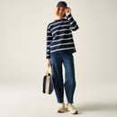Full-length view of model in a navy-and-white striped long-sleeve top, blue jeans and trainers, holding a tote bag and wearing a navy cap.