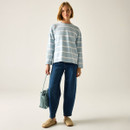 Full-length view of the model in the light blue and white striped long-sleeved top with dark blue jeans, holding a woven bag.