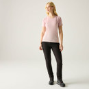 Woman wearing black hiking trousers with a pink short-sleeve top and walking boots, standing against a light studio background.