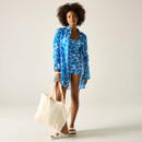 Woman wearing a blue floral print longline shirt and a swimming costume, styled with white sandals and a cream tote bag.
