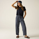 Woman wearing navy pinstripe trousers with a black short-sleeve top, styled with sandals and a bucket hat.