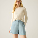 Model wearing light blue high-waisted shorts with a cream long-sleeve top, hands in pockets.