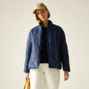 Model wearing a navy quilted jacket with a stand collar and zip front, styled with a beige cap and cream trousers.