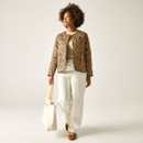 Full-length view of the model in a tan leopard-print quilted jacket, cream jeans and trainers, carrying a canvas tote bag.