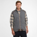 Man wearing a grey zip-up vest over a plaid shirt, standing against a plain white background. He has a neutral expression and casual pose.