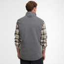 A man with short brown hair wearing a grey fleece vest over a plaid shirt, facing away. The tone is casual and relaxed, set against a plain background.