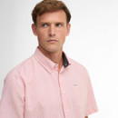 A man wearing a pink button-down shirt with a checkered pattern, looking to the side with a thoughtful expression. The shirt has a small logo on the pocket.