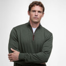 A person in a green quarter-zip jumper stands with arms crossed against a neutral background, conveying a calm and confident demeanour.
