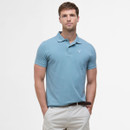 A man in a light blue polo shirt and beige pants stands against a plain white background with a neutral expression, conveying a casual and relaxed tone.