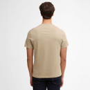Man in a beige t-shirt and dark jeans, standing with his back to the camera against a plain white background, conveying a casual, relaxed vibe.