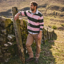 Man in a striped rugby shirt leans on a stone wall, gazing into the distance. Rolling hills in the background suggest a peaceful countryside setting.