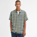 Man wearing a short-sleeve plaid shirt with green and blue tones, stands confidently against a plain white background, conveying a casual, relaxed vibe.