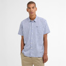 Man wearing a blue and white checkered short-sleeve shirt with beige pants, standing against a white background, conveying a casual and relaxed vibe.