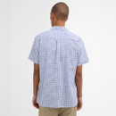 A person with a shaved head is viewed from the back, wearing a short-sleeved, blue and white checkered shirt with khaki pants against a plain background.