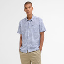 Young man in a short-sleeved, blue and white checkered shirt with hands in pockets of beige pants, standing against a plain white background. Casual and relaxed.