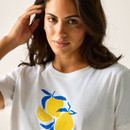 Close-up of a woman wearing a white T-shirt with a lemon and leaf graphic, showing the neckline and print detail.