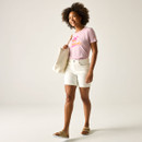 Full-length view of a woman wearing a light pink graphic T-shirt, white shorts and sandals, carrying a cream tote bag.