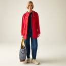 Full-length view of a woman wearing a red waterproof jacket over a dark top and blue jeans, carrying a striped tote bag.
