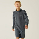 Young boy with short blond hair wearing a grey fleece jacket and matching shorts, standing against a neutral background, smiling confidently.