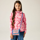 A young girl with long brown hair wearing a pink floral jumper, blue jeans, and a striped crossbody bag smiles softly against a neutral background.