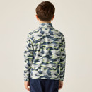 Rear view of a child wearing a blue and green camouflage-patterned jacket and dark pants, standing against a plain background. The mood is casual.