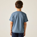 A young boy stands with his back to the camera, wearing a light blue t-shirt and dark shorts. The background is a plain off-white, creating a calm tone.