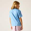 Young person with long blonde hair wearing pink sunglasses and a light blue t-shirt, facing away. They're in pink cargo shorts against a neutral background.