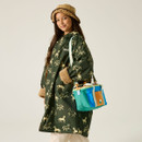 A woman in a green coat with horse patterns and fur cuffs smiles while holding a colorful bag. She's wearing a tan bucket hat. The mood is cheerful.