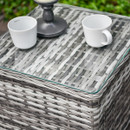 Close-up of grey rattan garden side table with glass top, showing woven texture and tabletop detail.