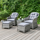 Grey rattan garden armchairs with matching footstools and a side table on a wooden deck, with grey cushions in a leafy garden setting.