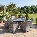 Grey rattan Florida 6 seater garden dining set with glass table and cushioned chairs on patio in landscaped garden