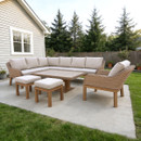 Outdoor patio with beige cushioned wicker furniture set on a concrete slab. Background features a quaint house and lush green trees, creating a cosy atmosphere.