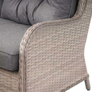 Close-up of a wicker armchair with grey cushions, highlighting the textured weave and soft fabric. The scene conveys comfort and rustic elegance.