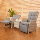 Two grey cushioned wicker recliners with matching footrests are positioned around a small wicker table with teacups. Wooden panel walls and a potted plant add warmth.
