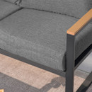 Close-up of a modern outdoor sofa with a gray cushion, black metal frame, and wood-topped armrest, set against a textured light brown rug.