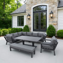 Outdoor patio with a sleek grey sectional sofa set around a rectangular table. Stone facade and greenery create a modern and inviting atmosphere.