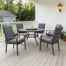 Cosy outdoor patio with a round table and five padded grey chairs on a wooden deck. Surrounded by white railings and a lush green garden.