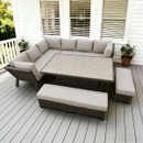Outdoor patio with white wooden decking features a light grey sectional sofa and matching benches around a rectangular table. Two potted plants add greenery.