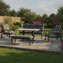 Kettler Tudor garden sofa set on a stone patio with three-seat sofa, two armchairs, padded bench and wood-effect adjustable table, surrounded by lawn and flowering borders.