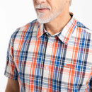Close-up of cream, orange and navy check shirt showing button-up collar and embroidered logo on chest.