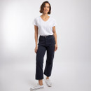 Woman wearing navy cropped jeans and a white V-neck T-shirt, standing in white trainers.