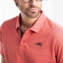 Close-up of coral-pink piqué polo shirt showing collar, buttons and embroidered chest logo.