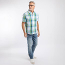 Man wearing a teal, blue and yellow check short-sleeve shirt with light blue jeans and trainers, standing in a studio.