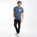 Man wearing a blue graphic T-shirt with small chest print, paired with black jeans on a white background.