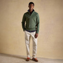 Model wearing a green quarter-zip fleece, cream trousers, and brown trainers, standing casually against a neutral studio backdrop.
